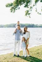 Sommer- Porträt von ein schön jung Familie mit zwei Kinder in der Nähe von das See. Mutter, Papa, Sohn und Tochter foto