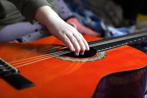 Kinderhand zieht die Saiten auf einer orangefarbenen Akustikgitarre foto