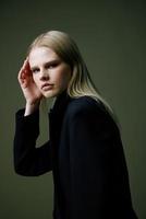 ein schließen Porträt von ein blond suchen Über ihr Schulter im ein schwarz Jacke posieren im ein Studio auf ein Grün Hintergrund. das Konzept von stilvoll Mode Fotografie foto