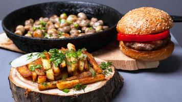 Pommes Frites, Burger und gebratene Pilze auf grauem Hintergrund, Nahaufnahme foto