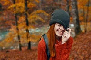 Frau im ein Hut und ein Sweatshirt mit ein Rucksack auf ihr zurück Spaß Herbst Landschaft Fluss foto