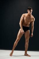 sportlich Mann mit ein muskulös Körper im schwarz kurze Hose posieren dunkel Hintergrund foto