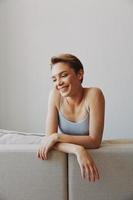 glücklich Frau Lächeln Lügen beim Zuhause auf das Couch entspannend auf ein Wochenende beim Zuhause mit ein kurz Haarschnitt Haar ohne Filter auf ein Weiß Hintergrund, kostenlos Kopieren Raum foto