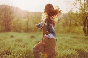 ein Frau Laufen durch ein Feld auf ein Sommer- Tag mit lange fließend Haar im das Strahlen von das Rahmen Sonne. das Konzept von Freiheit und Harmonie mit Natur foto
