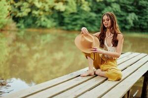 ein jung Hippie Frau sitzt auf ein See Brücke tragen stilvoll Öko Kleider und lächelnd foto