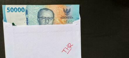 ein Weiß Briefumschlag geschrieben von thr und Neu indonesisch Banknoten, in der Regel Tunjangan Hari raya oder namens thr sind gegeben zu Angestellte voraus von eid. foto