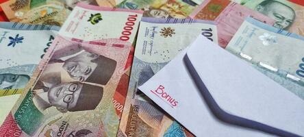 schließen oben Aussicht von ein Weiß Briefumschlag geschrieben von Bonus und Neu indonesisch Banknoten, in der Regel Tunjangan Hari raya oder namens thr sind gegeben zu Angestellte voraus von eid. Geld Rupiah Hintergrund foto