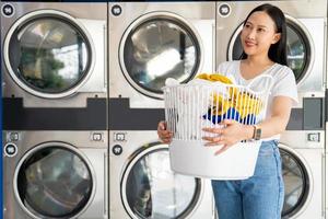 glücklich asiatisch Reinigung Frau tun Wäsche im ein Wäsche Geschäft. foto