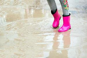 Nahansicht von Baby Füße im Rosa Gummi Stiefel im ein Pfütze. das wenig Mädchen fühlt sich geschützt von das Regen im Rosa Stiefel. foto