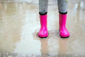 Nahansicht von Baby Füße im Rosa Gummi Stiefel im ein Pfütze. das wenig Mädchen fühlt sich geschützt von das Regen im Rosa Stiefel. foto