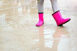 Nahansicht von Baby Füße im Rosa Gummi Stiefel im ein Pfütze. das wenig Mädchen fühlt sich geschützt im Rosa Stiefel. foto