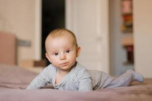 klein Baby Junge Lügen auf Bauch und erziehen seine Kopf während suchen überrascht, Neugeborene foto