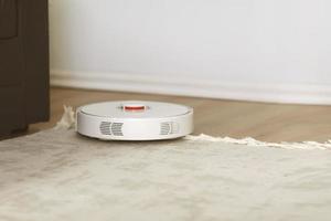 weißer Roboterstaubsauger auf einem Teppichreinigungsstaub im Wohnzimmerinnenraum. intelligente elektronische Housekeeping-Technologie. geringe Tiefe. foto