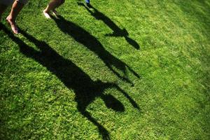 Silhouette von drei Personen, die mit ihren Händen auf grünem Gras gestreckt stehen foto