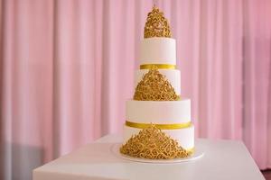 Hochzeitstorte mit Gold. Hochzeitstorte auf weißem Tisch. 3 Ebenen mit Elfenbeinfondant überzogen, besprüht mit Perlenspray und gelben Rosen aus Zuckerpaste. foto