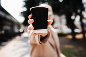 Mädchen, das eine Pappbecher Kaffee in ihren Händen nah oben zeigt foto