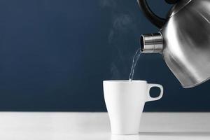 Tasse Tee mit Dampf, der heißes Wasser in eine Tasse auf einem dunklen Hintergrund gießt foto