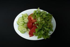 ein Foto von Gurken, Tomaten und Grüner Salat auf ein Teller auf isoliert schwarz Hintergrund Papier, nach etwas bearbeitet.