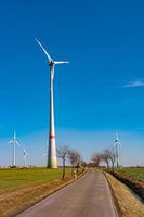 Aussicht Über schön Bauernhof Landschaft mit früh Frühling Landwirtschaft Feld, Wind Turbinen zu produzieren Grün Energie und ein einsam Straße in der Nähe von mittweida, Deutschland, beim Blau sonnig Himmel. foto