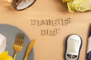 Diabetes Diät Text mit Teller und Besteck, Glucose Meter auf Beige Hintergrund eben legen, oben Aussicht foto