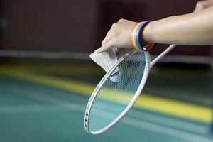 Badminton Spieler trägt Regenbogen Armbänder und halten Schläger und Weiß Federball im Vorderseite von das Netz Vor Portion es zu Spieler im Ein weiterer Seite von das Gericht, Konzept zum lgbt Menschen Aktivitäten. foto