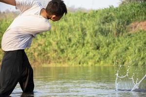 asiatisch Junge ist Ausgaben seine Freizeit durch Tauchen, Baden, werfen Felsen und fangen Fisch im das Fluss glücklich, Hobby und Glück von Kinder Konzept, im Bewegung. foto