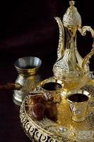 Stillleben mit traditionellem goldenen arabischen Kaffeeset mit Dallas, Kaffeekanne und Datteln. dunkler Hintergrund. vertikales Foto