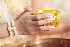 Frau Hand hoding Gold Tasse zum gießen Wasser im Muschel Schale auf glod Tablett im Tradition thailändisch Hochzeit Zeremonie foto