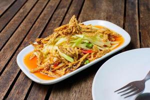 würzig Papaya Salat mit knusprig Fisch auf das hölzern Hintergrund. foto