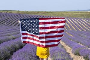 ein Mädchen mit ein amerikanisch Flagge im ein Lavendel Feld. amerikanisch Unabhängigkeit Tag. foto