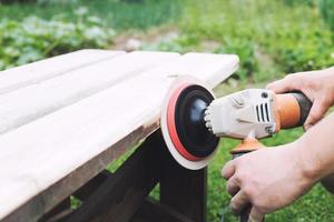 Mann poliert das Tafel auf das Bank. Mann reparieren Bank im das Garten foto