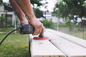 Mann poliert das Tafel auf das Bank. Mann reparieren Bank im das Garten foto