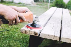 Mann poliert das Tafel auf das Bank. Mann reparieren Bank im das Garten foto