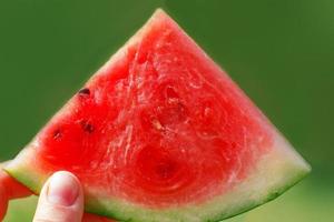 Hand halten Scheibe von Wassermelone isoliert auf ein Grün Hintergrund schließen foto