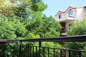 Aussicht von Balkon zu Grün Bäume und benachbart Haus mit Blau Himmel. ausruhen, Ruhe, Natur foto