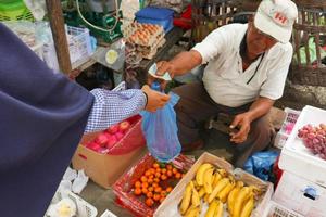 Surabaya, Osten Java, Indonesien, April 2, 2023, asiatisch Mann Verkauf Früchte im indonesisch traditionell Markt. Kauf und Verkauf Transaktionen durch Händler und Käufer foto