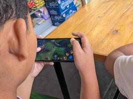 Surabaya, Indonesien - - April, 2023 - - ein asiatisch Junge spielen Handy, Mobiltelefon Legenden Spiele auf Smartphone foto