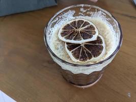 Arabica Kaffee Eis mit getrocknet Zitrone Scheibe mit Sahne schäumen. das Foto ist geeignet zu verwenden zum Kaffee Geschäft Hintergrund, Speisekarte Poster und Kaffee Inhalt Medien.