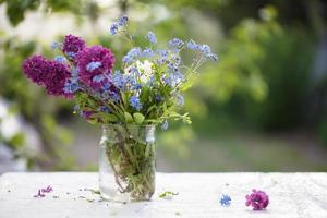 Frühling oder Sommer- Hintergrund. ein Strauß von Flieder und Vergissmeinnicht im ein Glas Krug auf das Tisch. schön Blumen auf ein Grün Hintergrund. foto