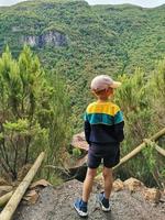 Junge steht mit seine zurück gegen Hintergrund von das Grün Berg. foto