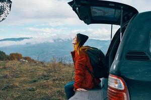 Frau Tourist mit ein Rucksack sitzt auf das Kofferraum von ein Auto im das Berge im Herbst im Natur foto