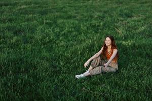 jung Frau spielen Spiele im das Park auf das Grün Gras Verbreitung ihr Waffen und Beine im anders Richtungen fallen und lächelnd im das Sonnenlicht von Sommer, ein Lebensstil von Leben und Jugend foto