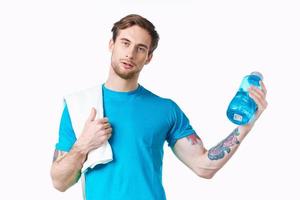 Sport Kerl im Blau T-Shirt mit ein Flasche von Wasser im das Fluss und tätowieren Weiß Hintergrund Fitness Modell- foto