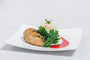 schwenken geröstet Hähnchen Brust mit lange Grün Bohnen und Licht Gemüse Reis Teller. Essen dekorieren mit rot Soße auf ein Weiß Platte. isoliert Weiß Hintergrund. foto