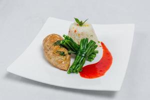 schwenken geröstet Hähnchen Brust mit lange Grün Bohnen und Licht Gemüse Reis Teller. Essen dekorieren mit rot Soße auf ein Weiß Platte. isoliert Weiß Hintergrund. foto