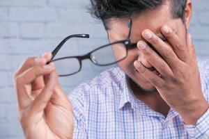 Mann nimmt die Brille ab, um den Kopf wegen Kopfschmerzen zu reiben foto