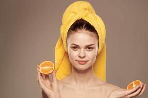 Frau mit Orangen im Hände Emotionen nackt Schultern Handtuch auf Kopf Beige Hintergrund foto