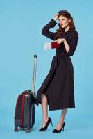 Frau im schwarz Mantel Koffer Reisepass und Flugzeug Fahrkarte Reise foto