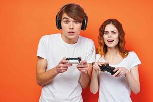 jung Paar im Weiß T-Shirts mit Joysticks spielen ein Konsole Orange Hintergrund foto