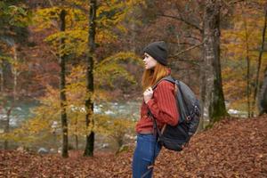 Frau mit Rucksack Gehen im das Herbst Park in der Nähe von das Fluss im Natur Seite Aussicht foto